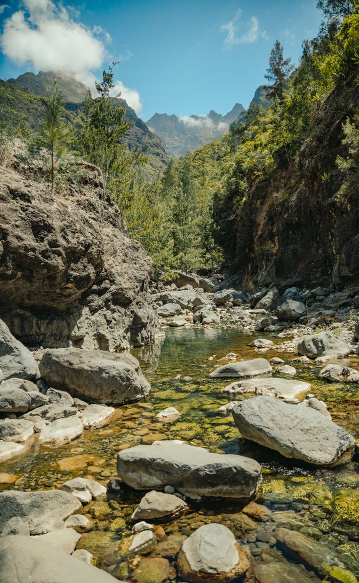 A tranquil stream surrounded by lush vegetation and rocky landscape in Cilaos, La Réunion.